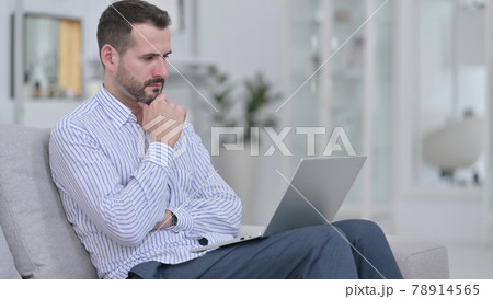 Pensive Young Man using Laptop at Home  78914565