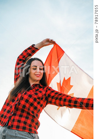 Young millennial brunette woman holding The National Flag of Canada. Canadian Flag or the Maple Leaf. Tourist traveler or patriotism. Immigrant in a free country. Independence day 1th july Young millennial brunette woman holding The National Flag of Canada. Canadian Flag or the Maple Leaf. Tourist traveler or patriotism. Immigrant in a free country. Independence day 1th july 78917055