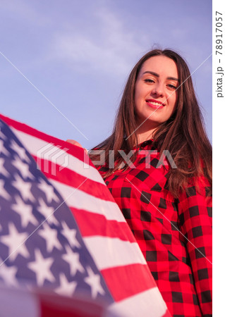 Young millennial brunette woman holding The National Flag of USA. American Flag. Tourist traveler or patriotism. Immigrant in free country. July 4th Independence Day. Caucasian Young millennial brunette woman holding The National Flag of USA. American Flag. Tourist traveler or patriotism. Immigrant in free country. July 4th Independence Day. Caucasian 78917057