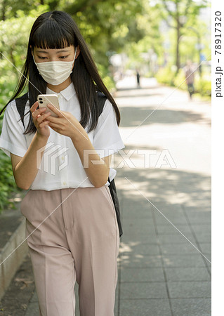 マスクをして歩きスマホをする10代女性 78917320