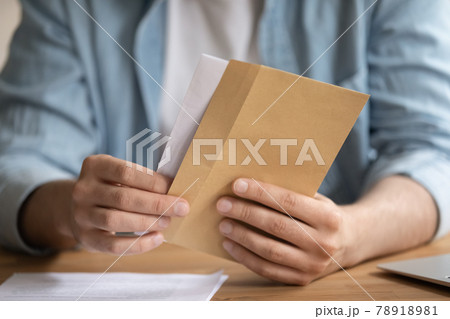 Close up young man opening envelope, feeling curious. 78918981