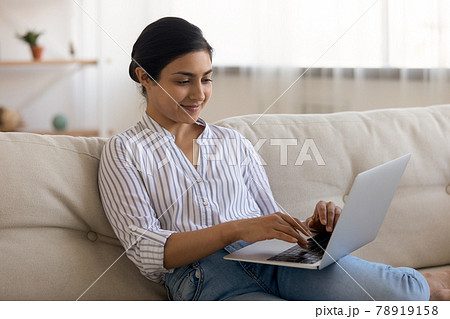 Happy Indian woman relax on sofa using laptop Happy Indian woman relax on sofa using laptop 78919158