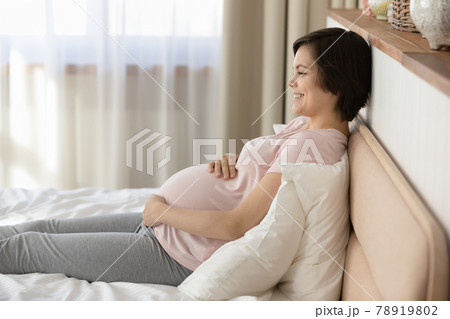 Side view smiling pregnant woman relaxing on bed, touching belly Side view smiling pregnant woman relaxing on bed, touching belly 78919802