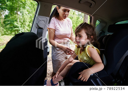 Cute female baby crying when mom puts her on the baby car seat. Safety of traveling in a car with children Cute female baby crying when mom puts her on the baby car seat. Safety of traveling in a car with children 78922534