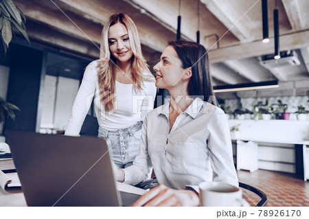 Two young female colleagues discussing business project together in office 78926170