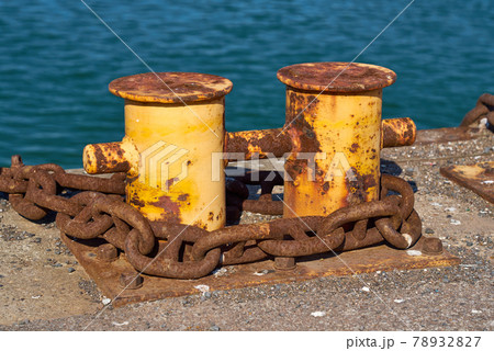 Side View of A double bitt mooring bollard with a heavy chain around it. 78932827