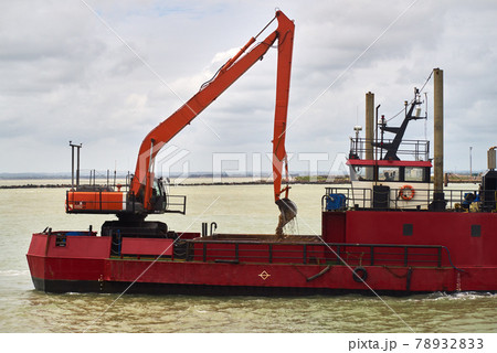 An excavator loads sand into a dredger 78932833