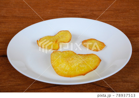 Dried and fried cassava slices place on white plate isolated on wood texture background. This is local Malaysian traditional junk food call Kerepek Ubi.  78937513