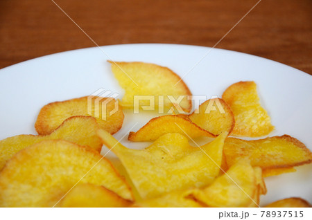 Dried and fried cassava slices place on white plate isolated on wood texture background. This is local Malaysian traditional junk food call Kerepek Ubi.  78937515