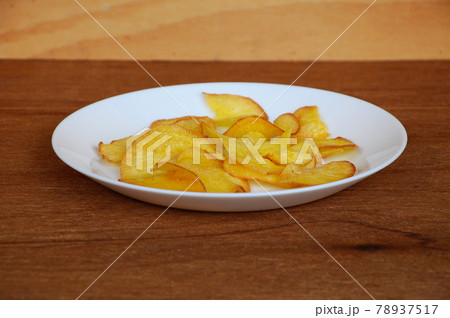 Dried and fried cassava slices place on white plate isolated on wood texture background. This is local Malaysian traditional junk food call Kerepek Ubi.  78937517