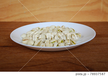 Plate of salted pistachio nuts on wood texture background.     78937587