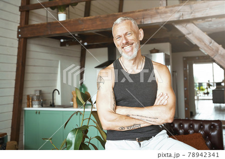 Portrait of a handsome cheerful caucasian mature man keeping arms crossed, smiling at camera while standing at his modern appartment 78942341