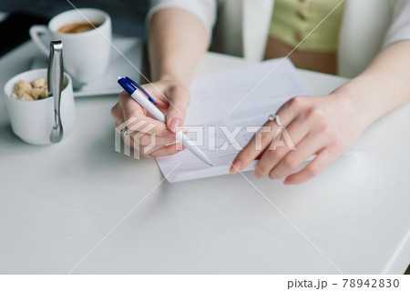 Young woman in white jacket working in cafe with papers, drinking coffee 78942830