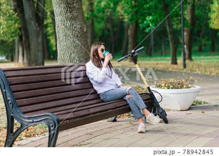 Young woman riding scooter in park sitting on bench 78942845