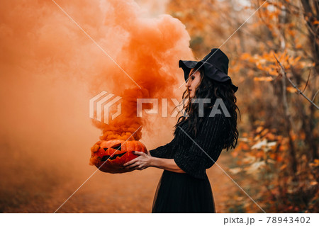 Orange smoke from pumpkin holding girl in witch costume Orange smoke from pumpkin holding girl in witch costume 78943402