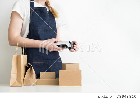 Woman holding modern payment terminal in hands with carton boxes, cardboard packages and kraft bag on the table 78943810