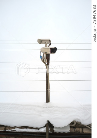 Two CCTV cameras stand on a snow-covered roof against a sky. Security concept. Two CCTV cameras stand on a snow-covered roof against a sky. Security concept. 78947683
