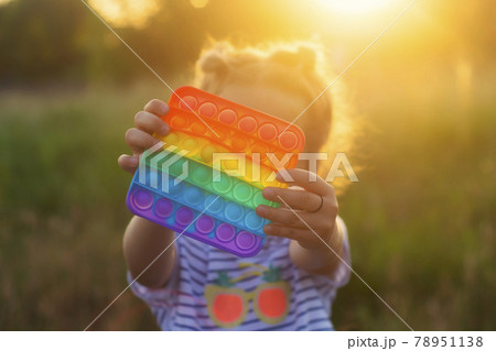 The child plays with a colorful rainbow game of poppit. Silicone fidget close-up. 78951138