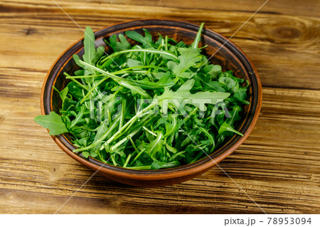 Fresh green arugula in ceramic bowl on a wooden table. Healthy food or vegetarian concept Fresh green arugula in ceramic bowl on a wooden table. Healthy food or vegetarian concept 78953094