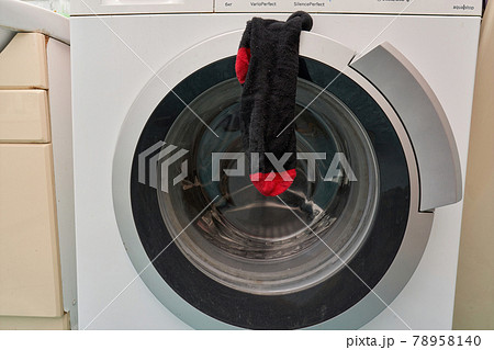 A clean black sock hangs on the door of the washing machine A clean black sock hangs on the door of the washing machine 78958140