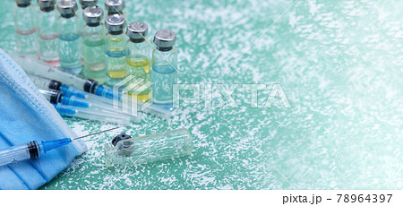 Medical ampoules, syringes and a mask on a green background. Vaccination against covid-19. 78964397