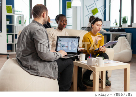 Businessman holding laptop with financial ghraphics while diverse employees talking Businessman holding laptop with financial ghraphics while diverse employees talking 78967585