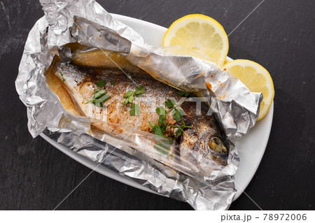 baked fish with lemon in aluminium foil on ceramic background baked fish with lemon in aluminium foil on ceramic background 78972006