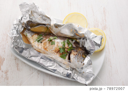 baked fish with lemon in aluminium foil on ceramic background baked fish with lemon in aluminium foil on ceramic background 78972007