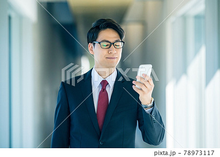 オフィスの廊下でスマホを見るスーツ姿の若いビジネスマン 78973117