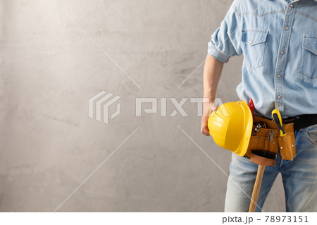 Man worker holding construction helmet and tool belt near wall. Male hand and construction tools 78973151