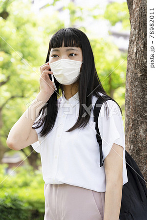 木の側でマスクをして電話をする少女 78982011