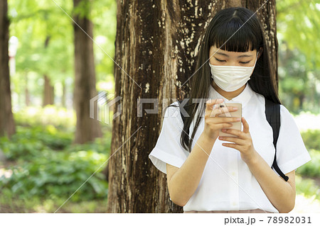 木の側でマスクをしてメールをする少女 木の側でマスクをしてメールをする少女 78982031