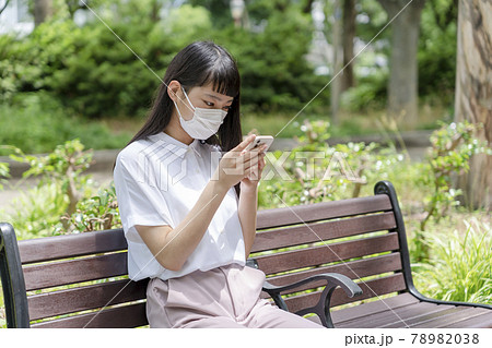 公園のベンチに座り マスクをしてスマホを操作する少女の写真素材 7038