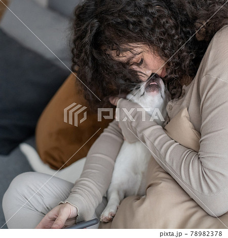 Cheerful curly woman kissing hugging little dog feeling love tenderness at cozy minimalistic home 78982378