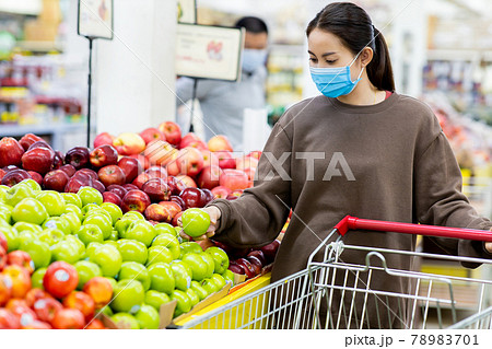 Young asian woman with protective mask pushing shopping cart for buying fresh Fruit in supermarket during virus COVID-19 outbreak. Concept for prevention COVID-19 Virus. Young asian woman with protective mask pushing shopping cart for buying fresh Fruit in supermarket during virus COVID-19 outbreak. Concept for prevention COVID-19 Virus. 78983701