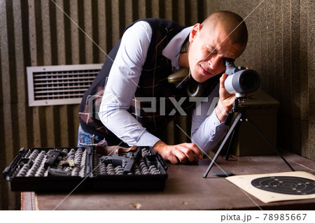 Instructor of shooting range looks through spyglass at target 78985667