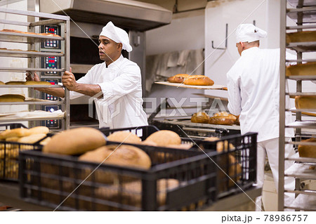 Confident baker carrying rack trolley with bread 78986757