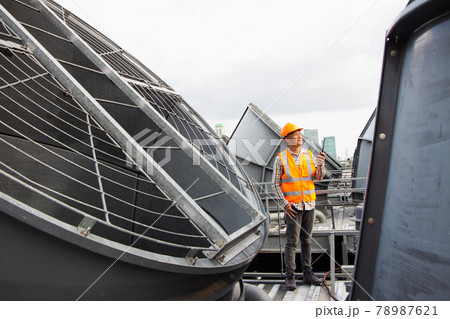Asian male engineer inspecting pipe fittings and chillers, refrigeration plant refrigeration plant in  factory. male mechanic wearing helmet and Reflective Safety Vest uses laptop, tablet, equipment 78987621