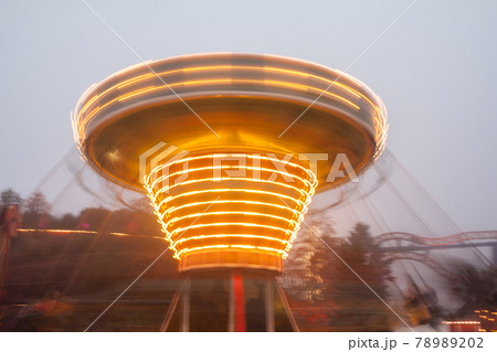 A blurry chain carousel in motion at the amusement park, evening illumination. The effect of bokeh and long exposure. A blurry chain carousel in motion at the amusement park, evening illumination. The effect of bokeh and long exposure. 78989202