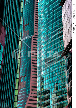 Details of close standing downtown buildings. Vertical lines, rhythm, reflections, cyan and reddish colors. Concept of business district architecture 78992024