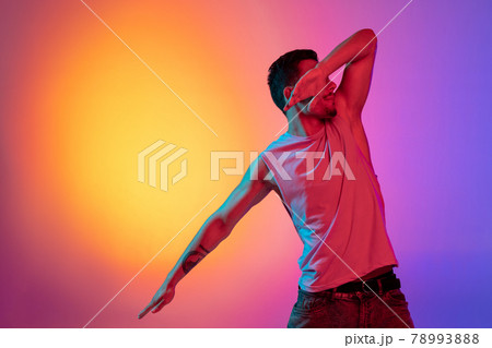 Portrait of Latina young man, dancer performing isolated on gradient yellow purple background in neon light. Concept of emotions, facial expression 78993888