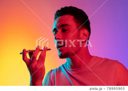 Portrait of Latina young man with phone, smartphone isolated on gradient yellow purple background in neon light. Concept of emotions, facial expression Portrait of Latina young man with phone, smartphone isolated on gradient yellow purple background in neon light. Concept of emotions, facial expression 78993903