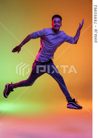 Full length portrait of Latina young man jumping high isolated on gradient yellow green background in neon light. Full length portrait of Latina young man jumping high isolated on gradient yellow green background in neon light. 78993962