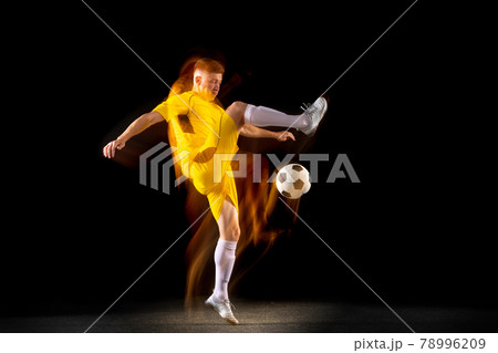 Young caucasian male football or soccer player kicking ball for the goal in mixed light on dark background. Concept of healthy lifestyle, professional sport, hobby. 78996209