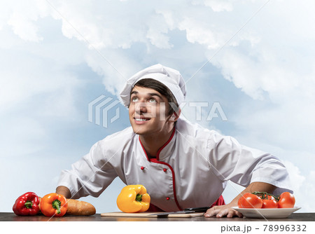 Young smiling chef standing near cooking table Young smiling chef standing near cooking table 78996332