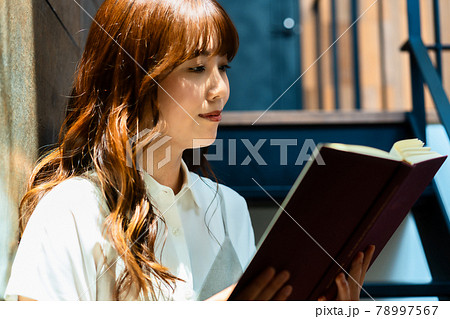日差し差し込む階段で読書をする女性 78997567