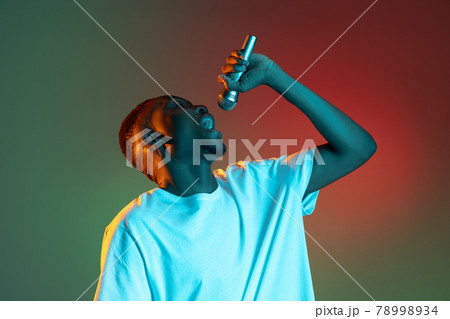 Young african man singing with microphone on neon gradient background. Concept of emotion, action, facial expression. 78998934