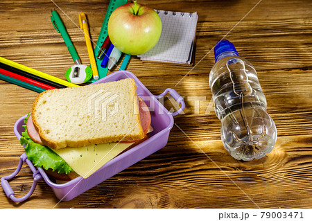 Back to school concept. School supplies, bottle of water, apple and lunch box with sandwiches on a wooden desk 79003471