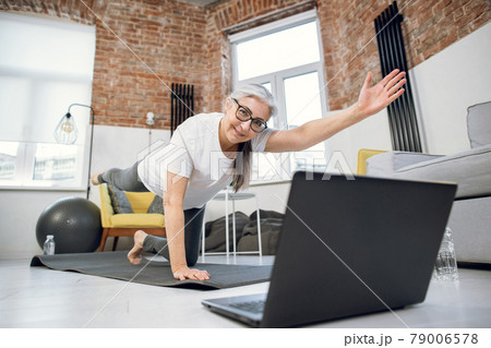 Retired woman using laptop and doing yoga at home Retired woman using laptop and doing yoga at home 79006578