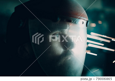 Man welder grinder in transparent protective mask with flying sparks in darkness. Man welder grinder in transparent protective mask with flying sparks in darkness. 79006865